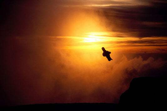 Snowboarder silhouetted against a golden sunset sky mid-jump