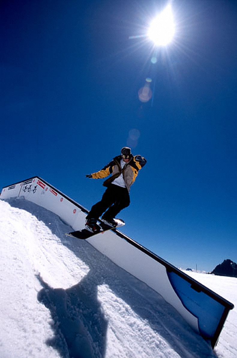 Snowboarder sliding a rail on a sunny day under a deep blue sky