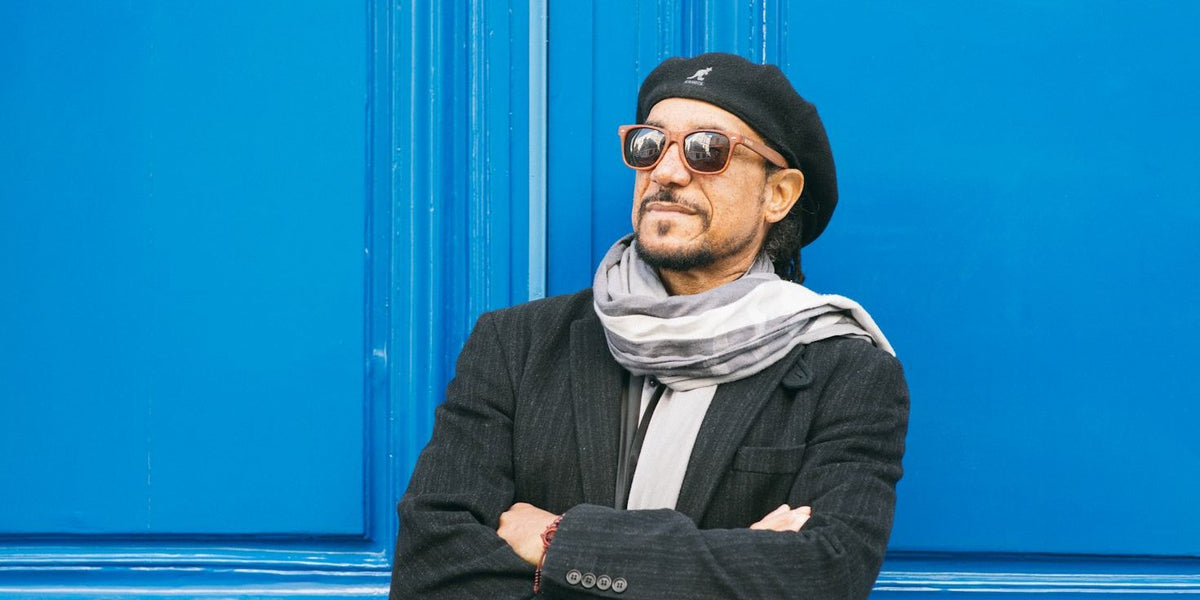 Man in a beret and sunglasses leaning against a bright blue door