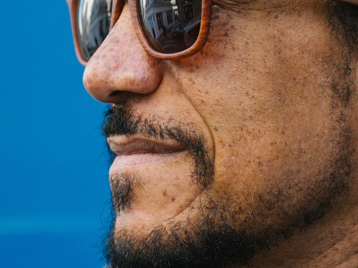 Close-up profile of a man wearing Lenoir wood-frame sunglasses with mirrored lenses